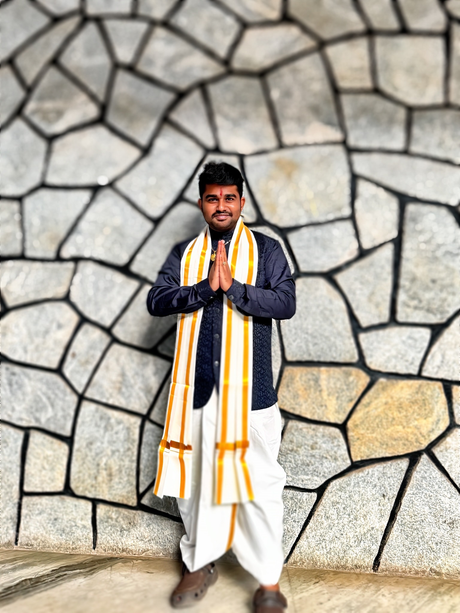 Roshan Rajkumar Sivakumar in traditional South Indian Tamil Nadu attire — white veshti and yellow angavastram — doing namaste pose at Bhasha Utsav Christ University Bengaluru 2024 annual language and culture festival