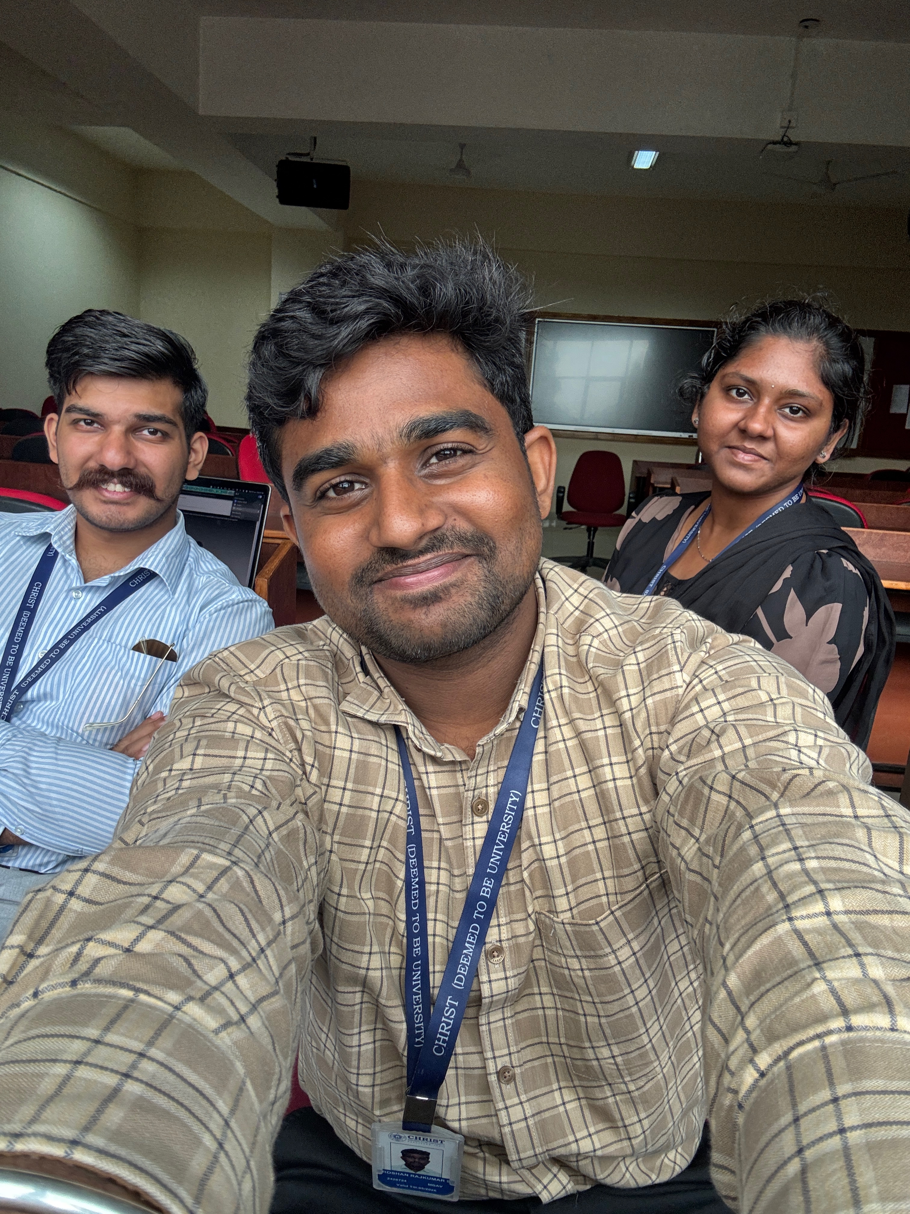 Roshan Rajkumar Sivakumar casual classroom selfie with friends at Christ University Bengaluru — MBA TVW batch 2024-26 with Christ University ID lanyards